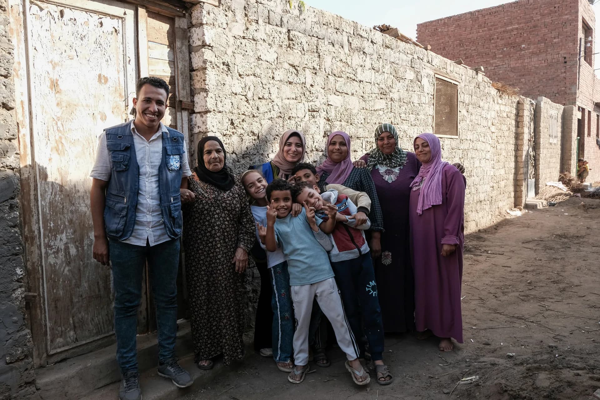 أحد أعضاء فريق مؤسسة ومن الماء حياة مع إحدى الأسر المستفيدة وأطفالها أمام منزلها في قرية بصعيد مصر